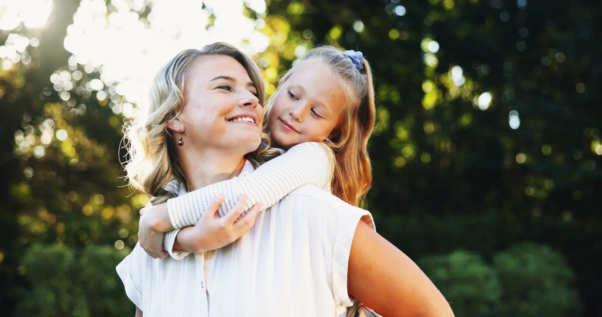A mother giving her daughter a piggyback ride outdoors, both laughing