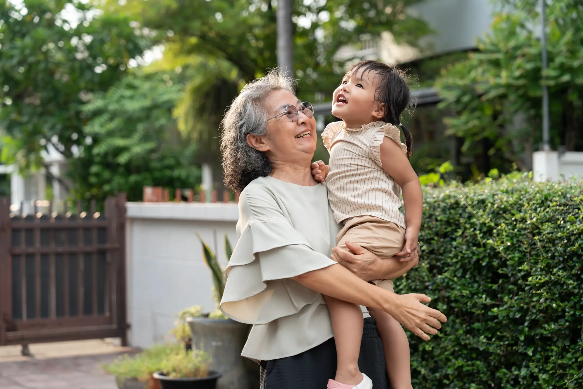 A grandmother laughing while holding her grandchild outdoors