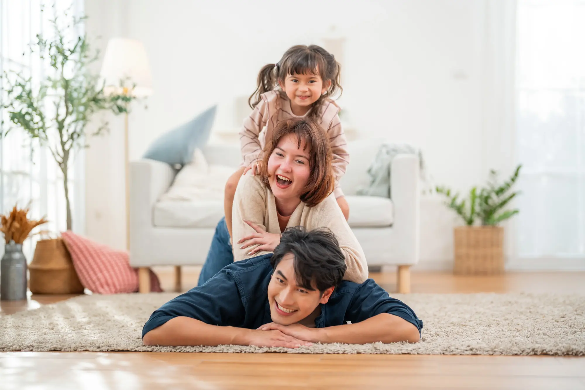 A father laughing with his two children piled on his back in a living room